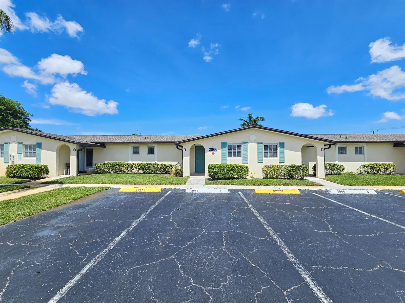 A single-story apartment building with a parking lot in the foreground under a blue sky — 2966 Ashley Drive E # F, West Palm Beach FL 33415, WEST PALM BEACH, FL