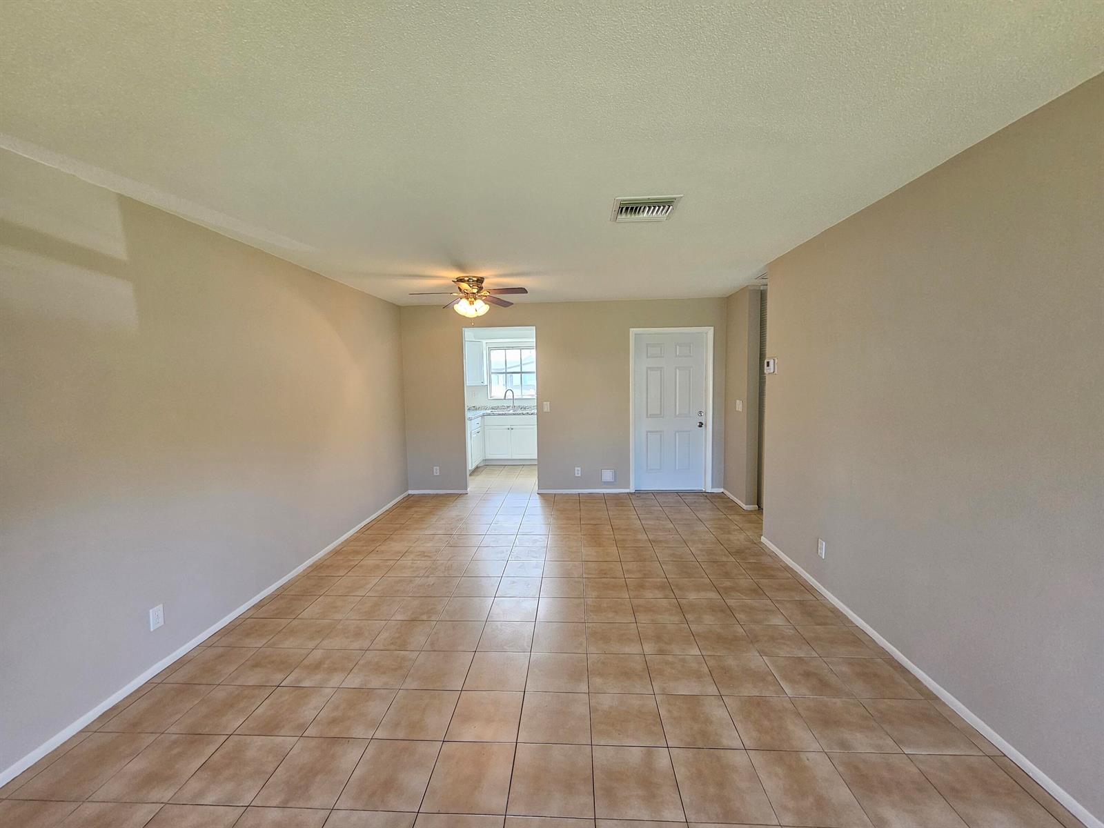 An empty living room with beige walls, tan tile flooring, and a ceiling fan — 2966 Ashley Drive E # F, West Palm Beach FL 33415, WEST PALM BEACH, FL