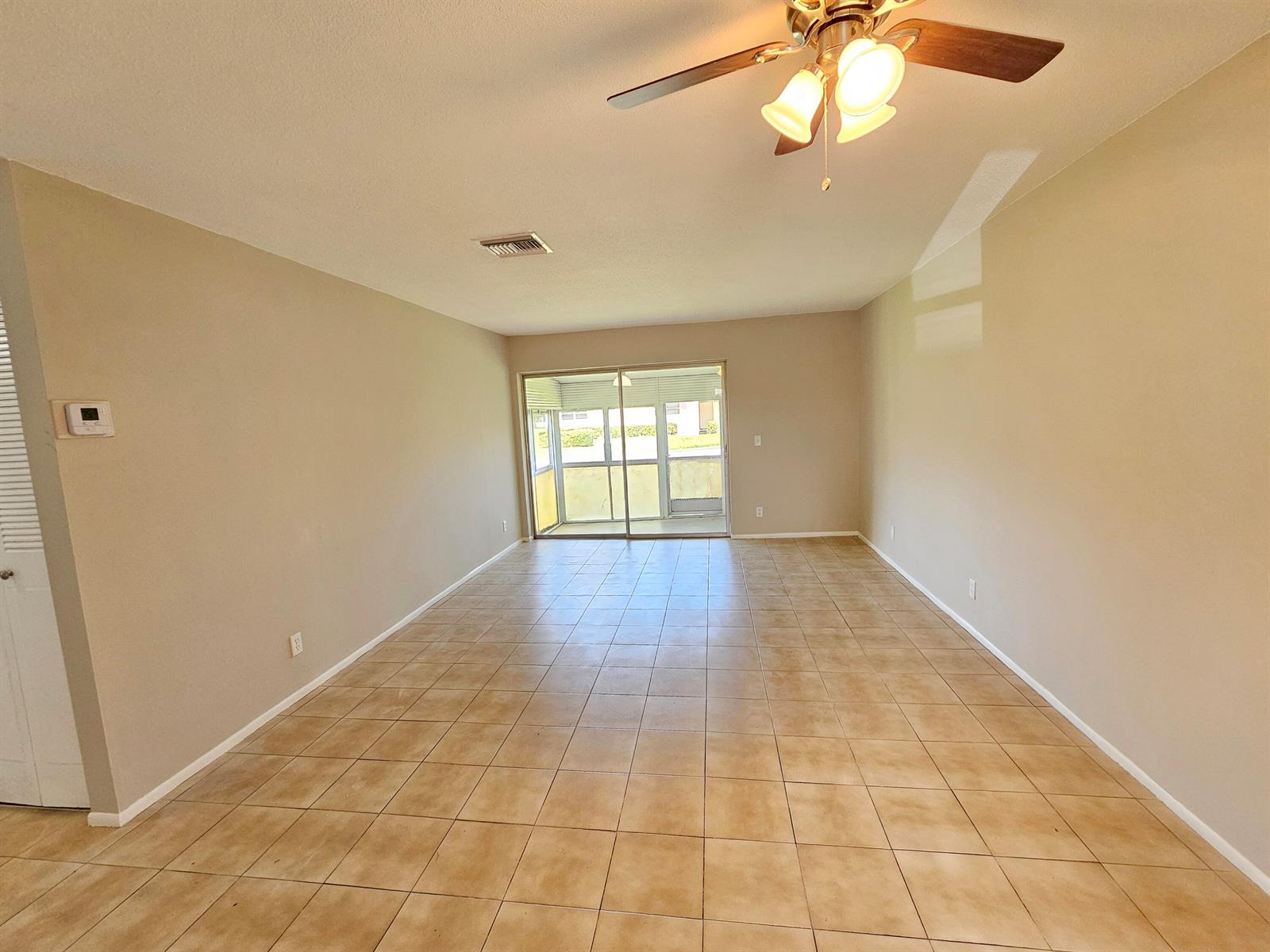 An empty living room features beige walls, tile flooring, a ceiling fan, and sliding glass doors — 2966 Ashley Drive E # F, West Palm Beach FL 33415, WEST PALM BEACH, FL
