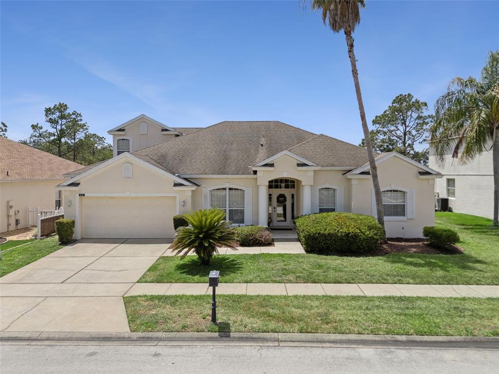 A single-story suburban house with a two-car garage, beige stucco exterior, and a palm tree — 117 N HAMPTON DRIVE, DAVENPORT, FL