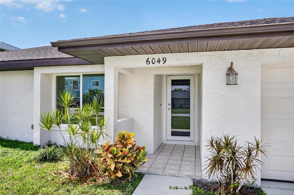 The exterior of a white house features a front door, a garage, and landscaping — 6049 PERTHSHIRE LANE, FORT MYERS, FL