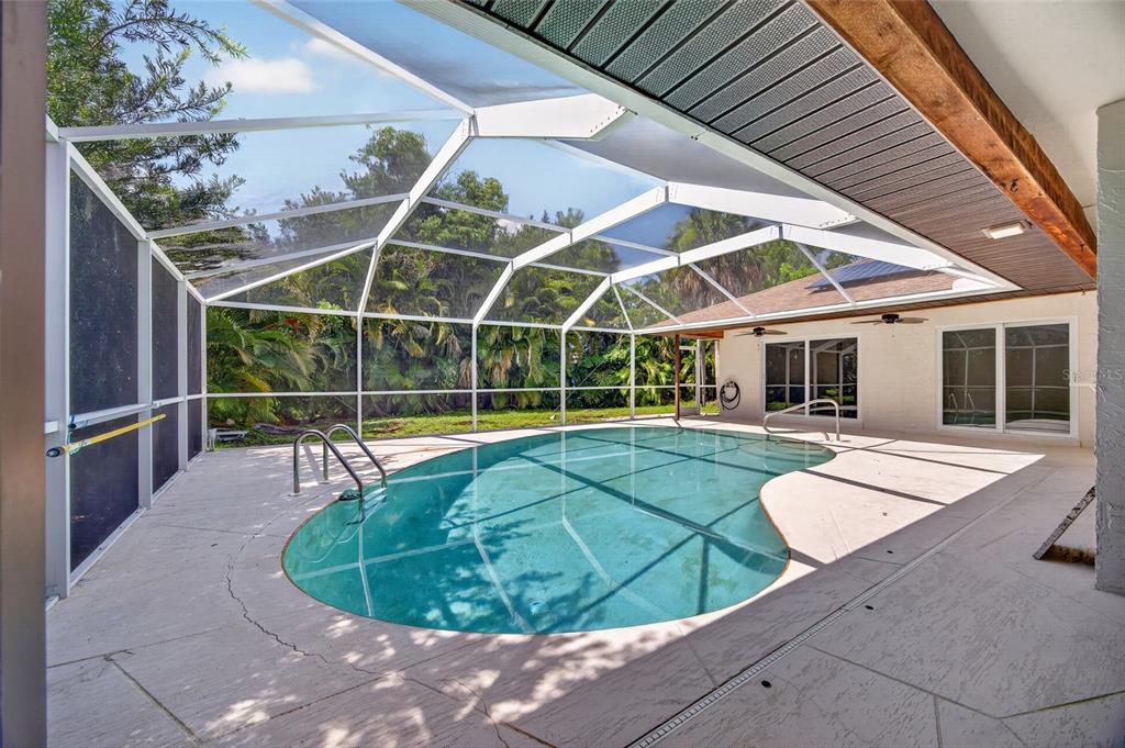 A kidney-shaped swimming pool sits inside a screened-in lanai with a concrete deck — 6049 PERTHSHIRE LANE, FORT MYERS, FL