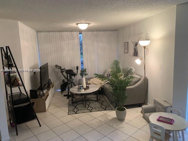 A living room features tile flooring, a grey sofa, a coffee table, and a stationary bike — 7035 NW 186th St # D310, Hialeah FL 33015, HIALEAH, FL