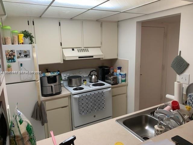 A kitchen features white cabinets, a white stove, a refrigerator, and a stainless steel sink — 7035 NW 186th St # D310, Hialeah FL 33015, HIALEAH, FL