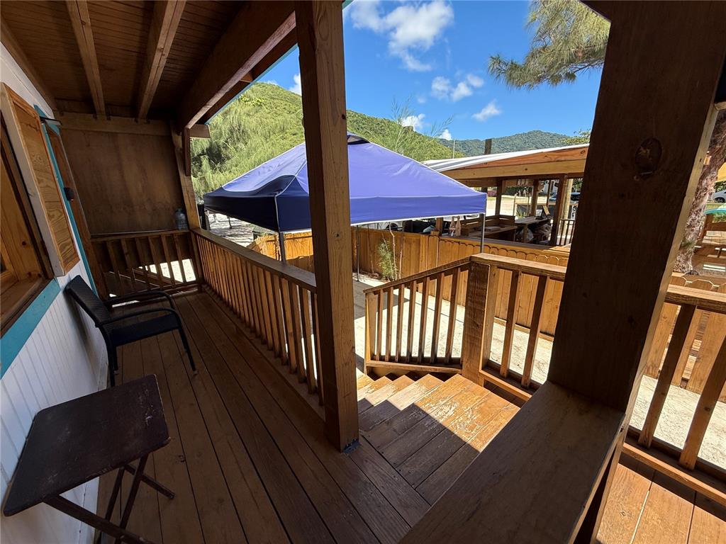A wooden deck with stairs leads down to a patio area featuring a blue canopy — CARR. #3 BEACH FRONT VILLA, PATILLAS, PR