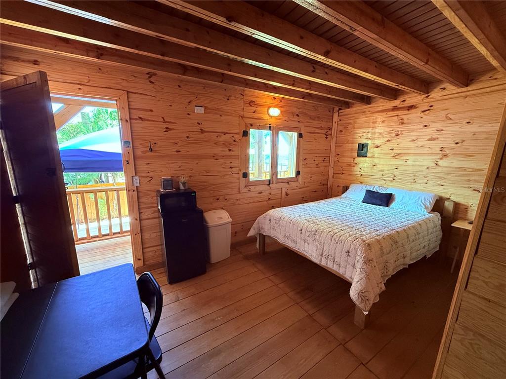 A rustic bedroom features wood-paneled walls, a bed, a small refrigerator, and an open door — CARR. #3 BEACH FRONT VILLA, PATILLAS, PR