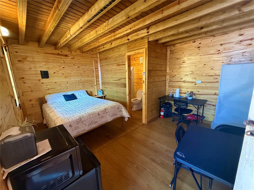 A rustic bedroom features wood-paneled walls, a bed, a small desk, and an attached bathroom — CARR. #3 BEACH FRONT VILLA, PATILLAS, PR
