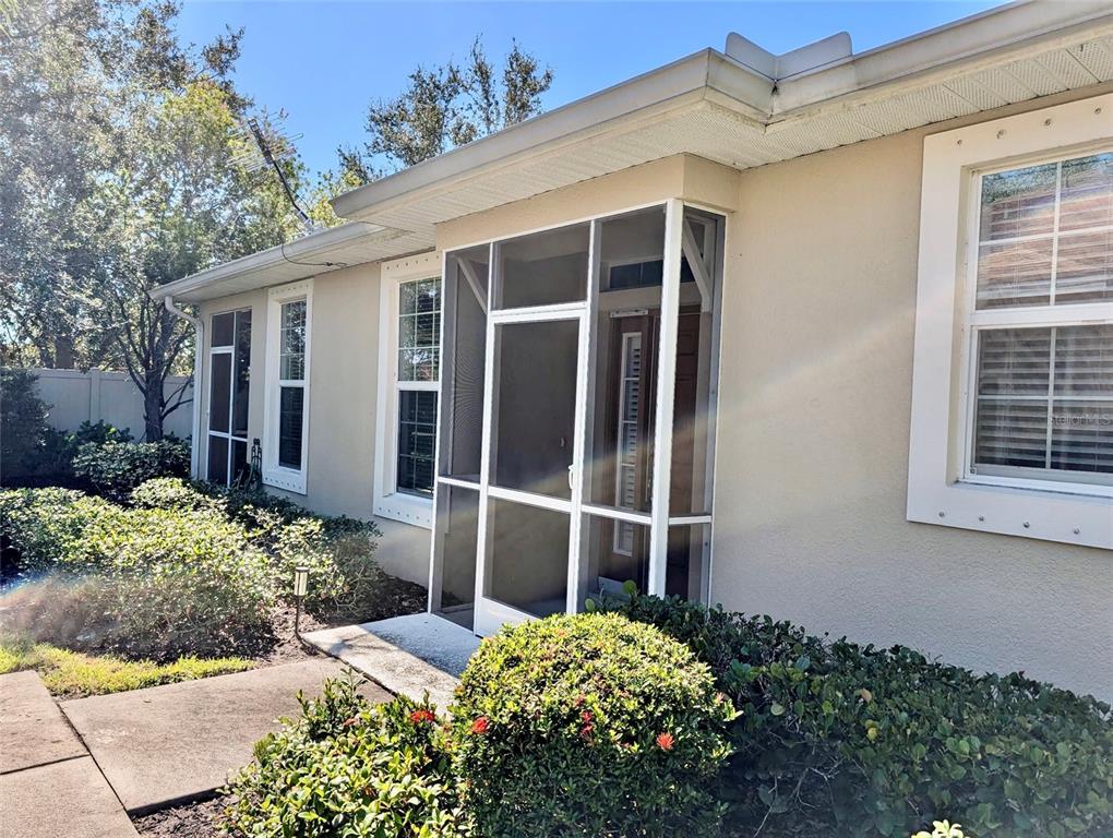 A beige house exterior features a white-framed screened entryway and several windows with shutters — 2585 CORTENOVA COURT, VENICE, FL