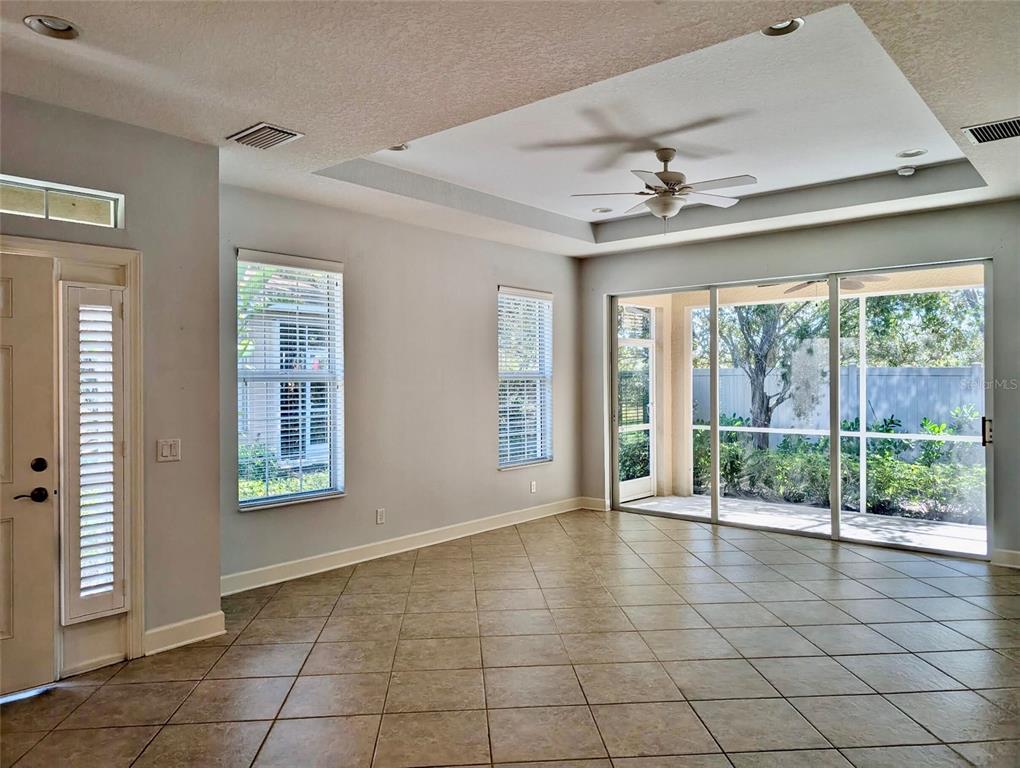An empty room features tile flooring, a tray ceiling with a fan, and sliding glass doors — 2585 CORTENOVA COURT, VENICE, FL