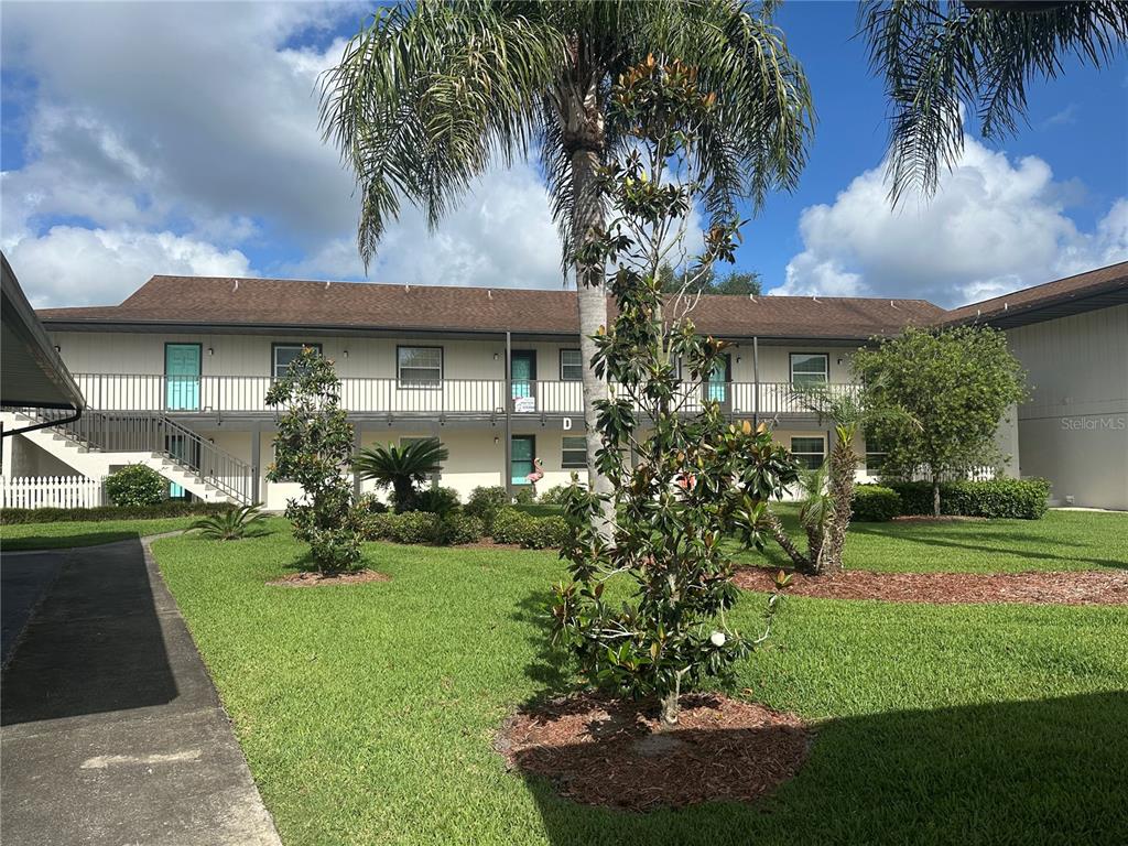 A two-story apartment building with a central courtyard, palm trees, and a grassy lawn — 1640 JUNO TRAIL UNIT 102D, ASTOR, FL