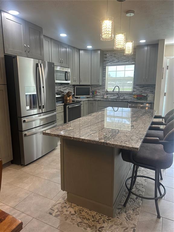 A kitchen features grey cabinets, stainless steel appliances, a granite island, and tiled flooring — 1640 JUNO TRAIL UNIT 102D, ASTOR, FL