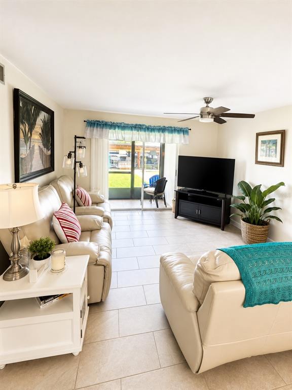 A living room features light-colored tile floors, leather seating, a television, and a sliding glass door — 1640 JUNO TRAIL UNIT 102D, ASTOR, FL