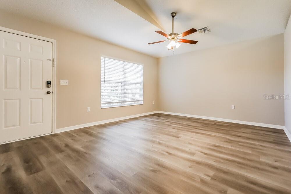 An empty room with light-colored walls, wood-look flooring, a ceiling fan, and a front door — 11730 LYNN BROOK CIRCLE, SEFFNER, FL