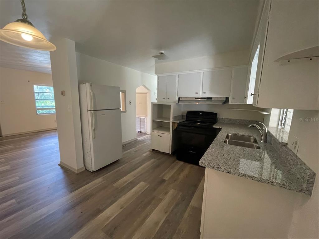 A kitchen features white cabinets, granite countertops, a black stove, and light wood-look flooring — 143 E SOUTH STREET, DELAND, FL
