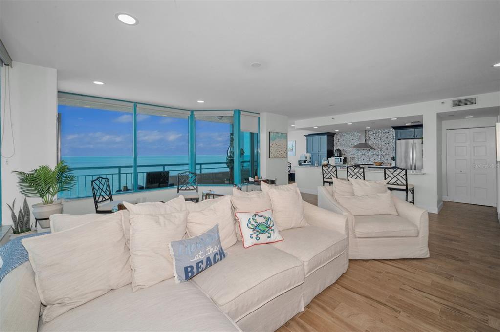 A living room with a large sofa, kitchen, and floor-to-ceiling windows overlooking the ocean — 1520 GULF BOULEVARD UNIT 1201, CLEARWATER BEACH, FL