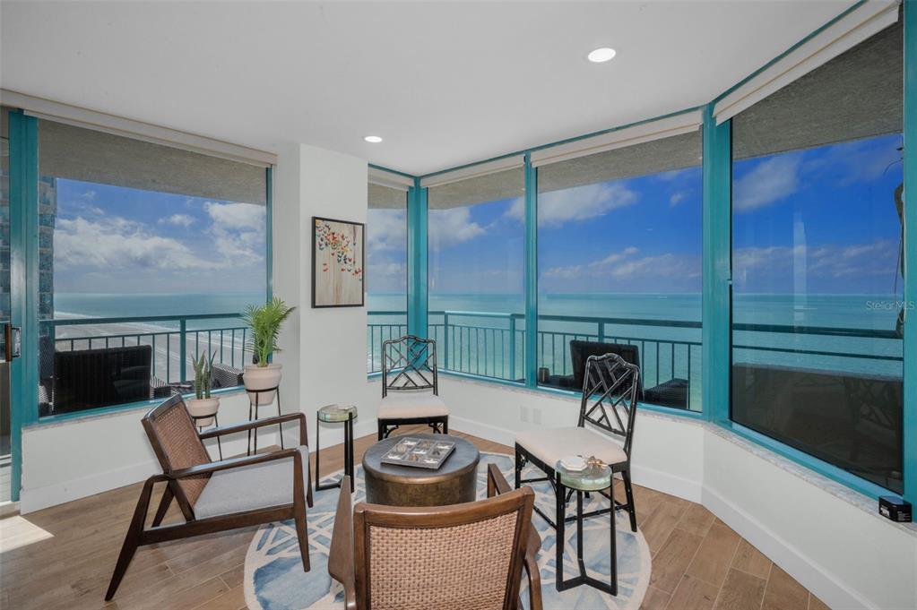 A sunroom with floor-to-ceiling windows overlooking the ocean, featuring wood-look flooring and patio furniture — 1520 GULF BOULEVARD UNIT 1201, CLEARWATER BEACH, FL