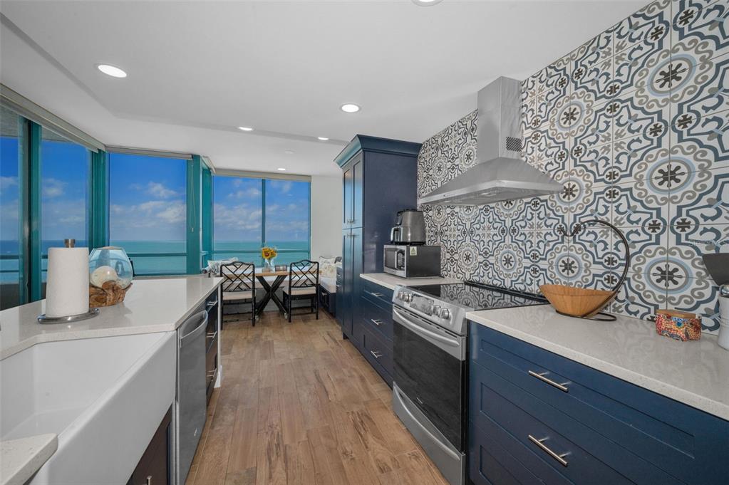 A kitchen with blue cabinets, patterned tile backsplash, and a view of the ocean — 1520 GULF BOULEVARD UNIT 1201, CLEARWATER BEACH, FL