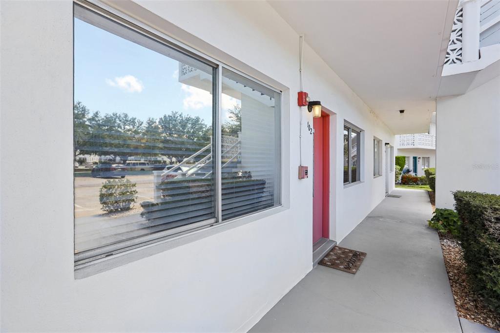 A white exterior walkway leads to a pink front door with a large adjacent window — 11225 82ND AVENUE UNIT 102, SEMINOLE, FL