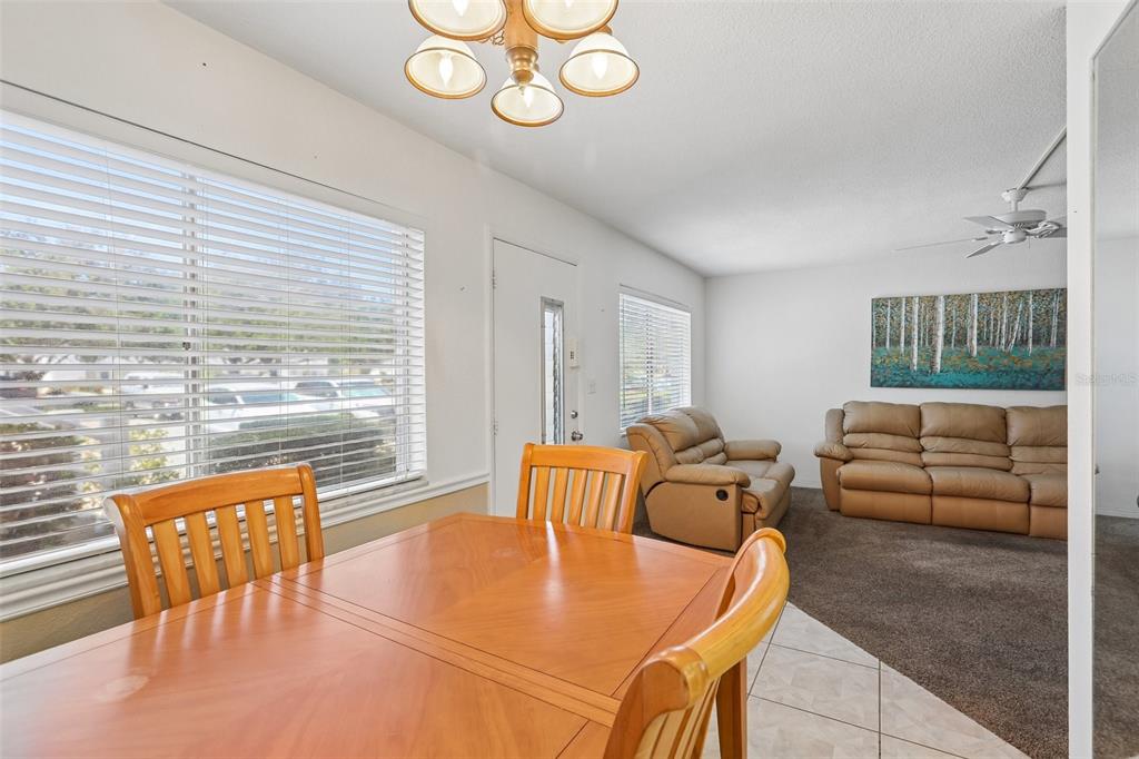 A dining area with a wooden table and chairs transitions into a carpeted living room — 11225 82ND AVENUE UNIT 102, SEMINOLE, FL