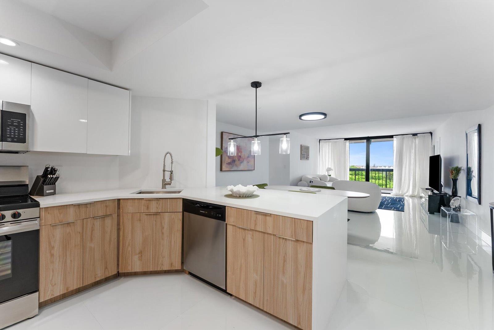 A modern kitchen with light wood cabinets and white countertops opens to a living area — 2425 Presidential Way # 704, West Palm Beach FL 33401, WEST PALM BEACH, FL