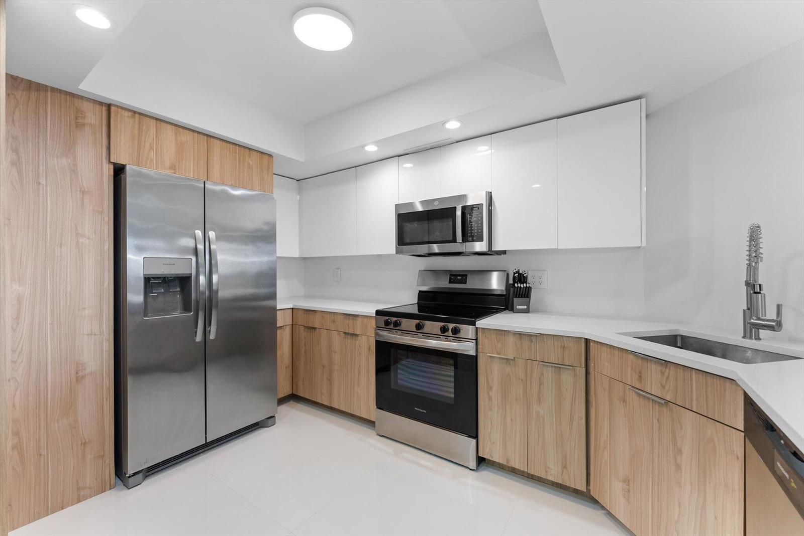 A modern kitchen features light wood cabinets, white upper cabinets, stainless steel appliances, and countertops — 2425 Presidential Way # 704, West Palm Beach FL 33401, WEST PALM BEACH, FL