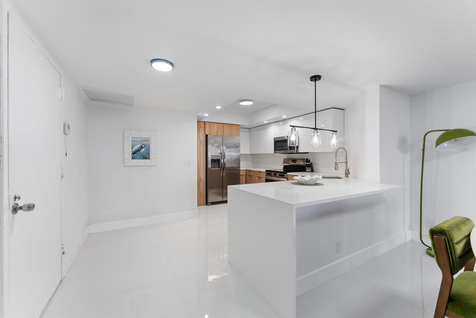 A modern kitchen features white cabinets, stainless steel appliances, a white island, and green chairs — 2425 Presidential Way # 704, West Palm Beach FL 33401, WEST PALM BEACH, FL