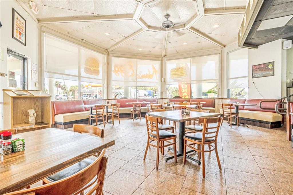 A restaurant dining area features tiled floors, wooden tables, chairs, and booths under a ceiling fan — 935 S ATLANTIC AVENUE, DAYTONA BEACH, FL