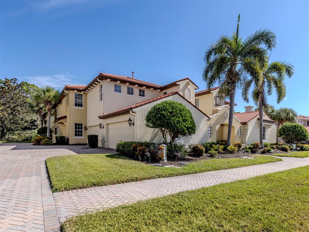 A two-story stucco house with a tile roof, palm trees, and a brick paver driveway — 122 BELLA VISTA TERRACE UNIT 8A, NORTH VENICE, FL