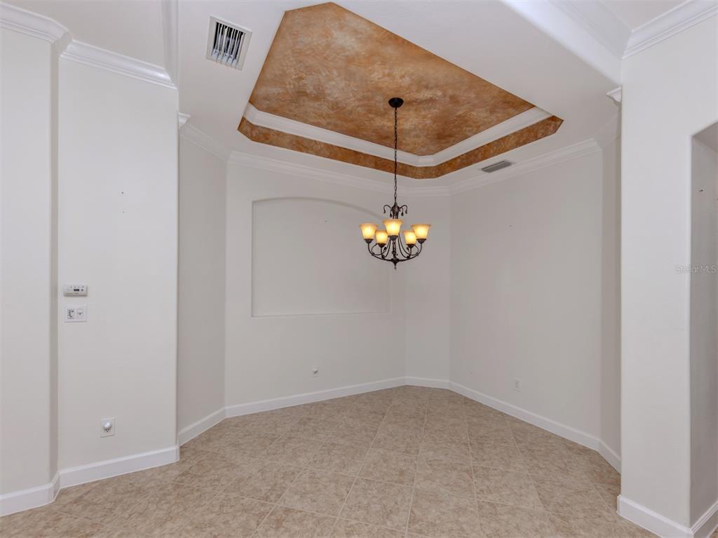 A dining room features a tray ceiling with a faux finish and a hanging chandelier — 122 BELLA VISTA TERRACE UNIT 8A, NORTH VENICE, FL