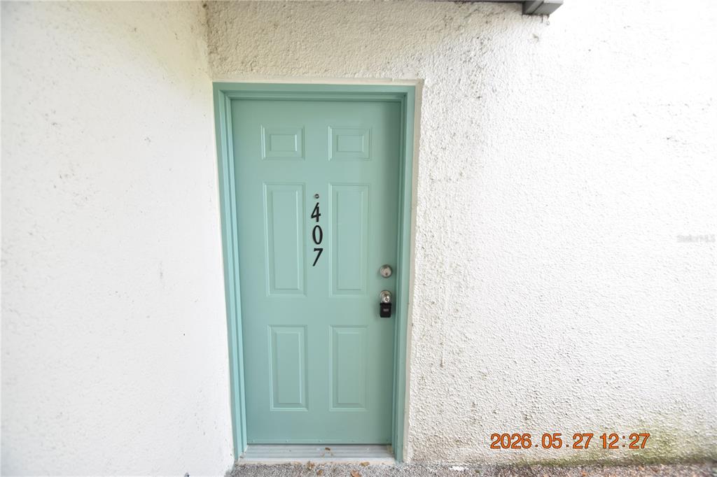 A light green front door with the number 407 is set into a textured white wall — 877 114TH AVENUE N UNIT 407, ST PETERSBURG, FL