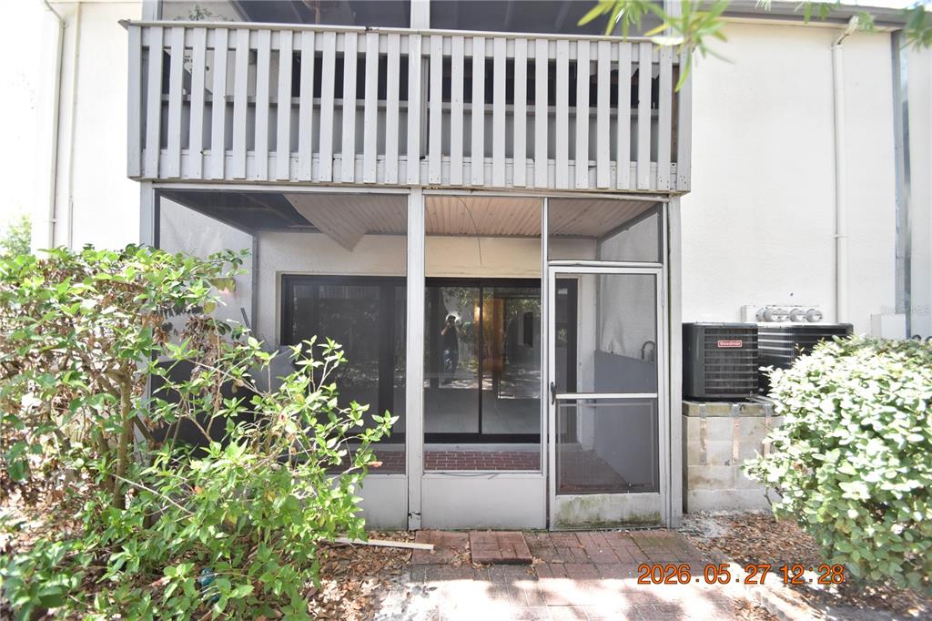 A ground-level screened-in patio with a brick floor and a second-story balcony above — 877 114TH AVENUE N UNIT 407, ST PETERSBURG, FL