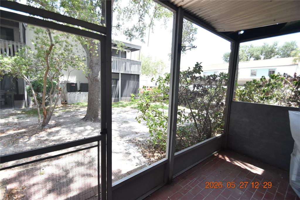 A screened-in porch with a brick floor overlooks a sandy yard and neighboring apartment buildings — 877 114TH AVENUE N UNIT 407, ST PETERSBURG, FL