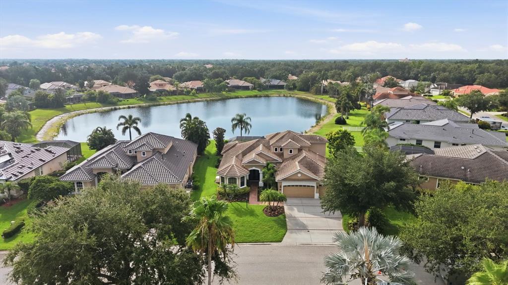 An aerial view shows a suburban house with a tile roof situated beside a lake — 6915 HONEYSUCKLE TRAIL, LAKEWOOD RANCH, FL