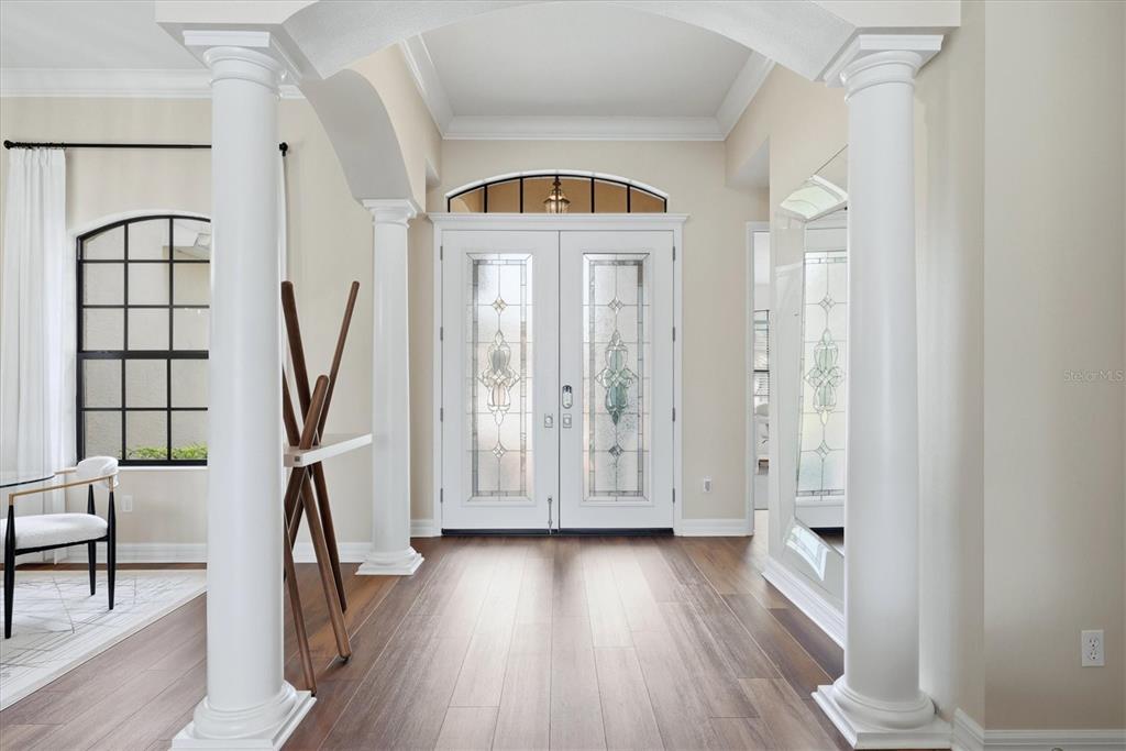A bright entryway features white columns, wood flooring, and double glass-paneled doors with an arched transom — 6915 HONEYSUCKLE TRAIL, LAKEWOOD RANCH, FL