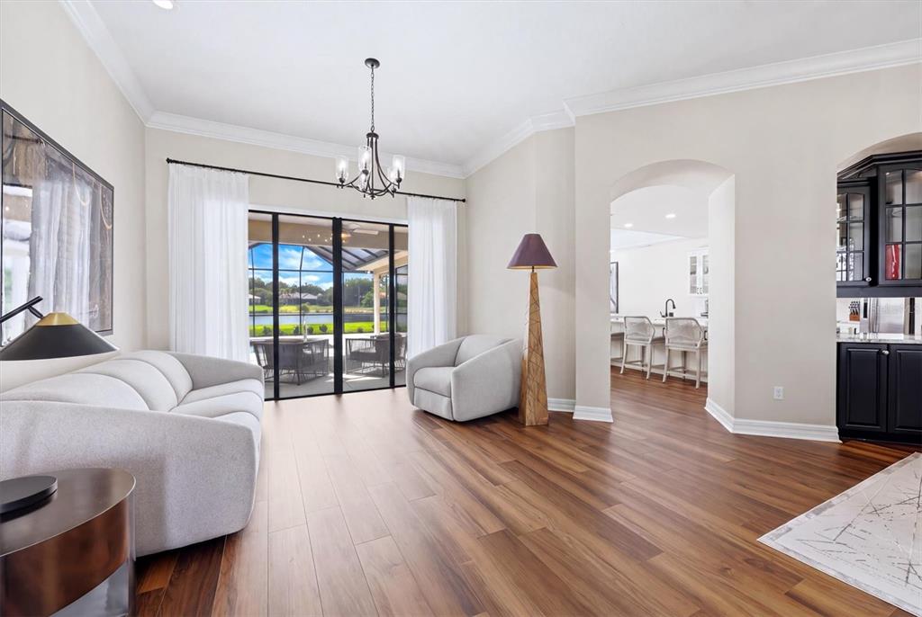 A living room with wood floors, a sofa, an armchair, and a view of a pool — 6915 HONEYSUCKLE TRAIL, LAKEWOOD RANCH, FL