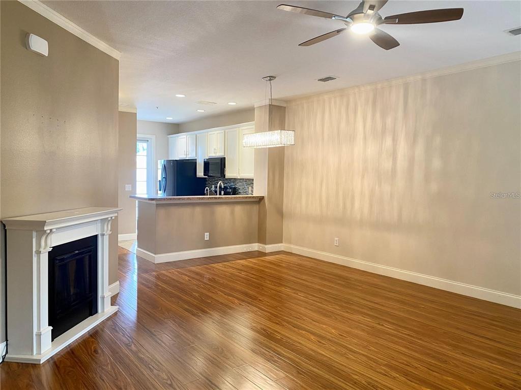 A living room with wood flooring and a fireplace opens to a kitchen with cabinets — 7975 NORTHLAKE PARKWAY, ORLANDO, FL