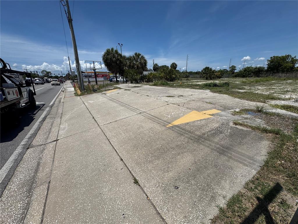 A paved driveway entrance with yellow directional arrows leads to an empty, grassy vacant lot — 8725 W WATERS AVENUE, TAMPA, FL