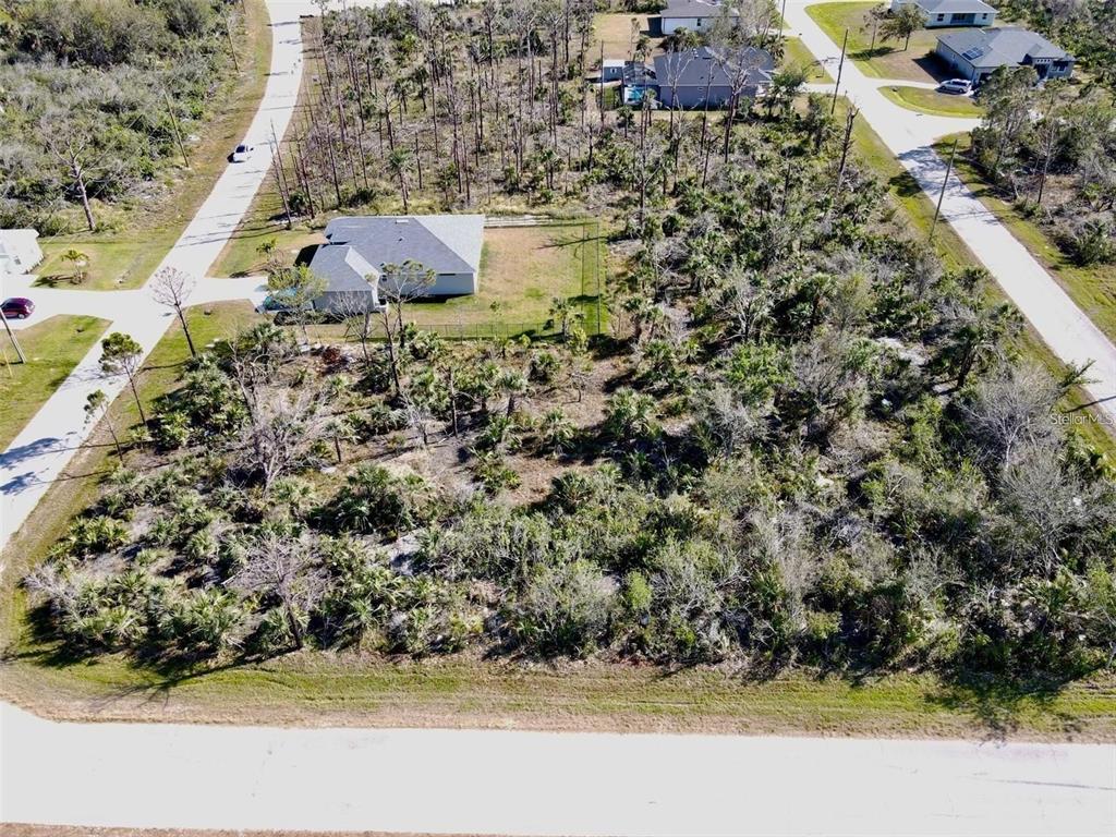 An aerial view shows a vacant, wooded residential lot next to a house and paved roads — 8045 THRUSO ROAD, PORT CHARLOTTE, FL