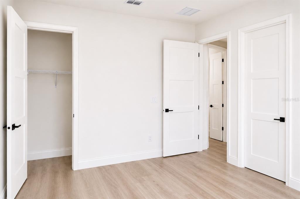 A room with light wood-look flooring, white walls, and three white doors with black hardware — 68 ERIC DRIVE, PALM COAST, FL
