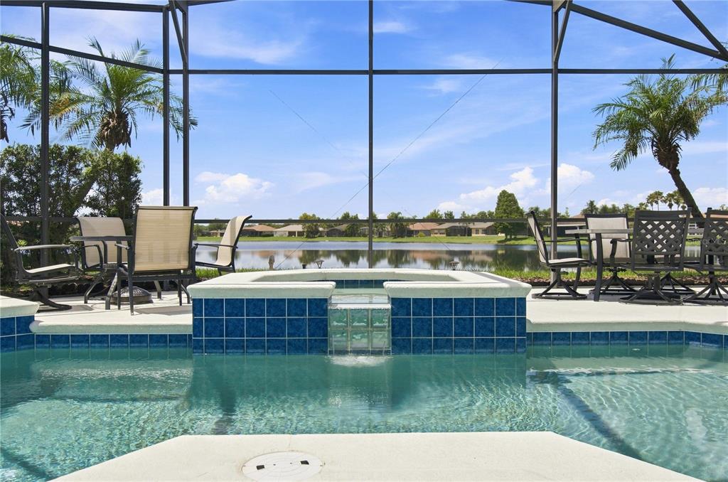 A swimming pool and spa with blue tile accents overlook a lake inside a screened enclosure — 662 SHOREHAVEN DR, POINCIANA, FL
