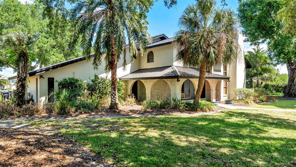 A two-story house with a metal roof and arched brick entryway sits on a lawn — 6037 CRICKET DRIVE, LAKELAND, FL