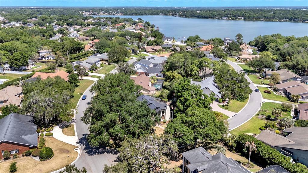 An aerial view shows a suburban neighborhood with houses, mature trees, and a large lake — 6037 CRICKET DRIVE, LAKELAND, FL