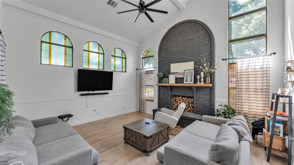 A living room features a vaulted ceiling, a black brick fireplace, and light wood flooring — 6037 CRICKET DRIVE, LAKELAND, FL