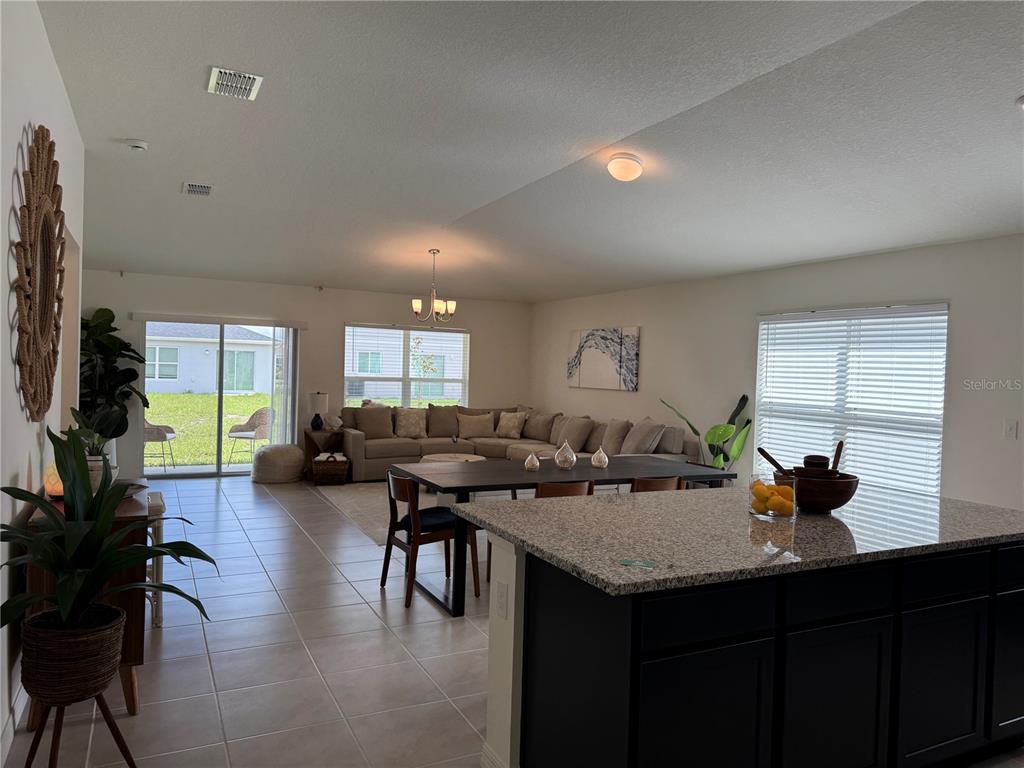 An open-concept living and dining area features tile flooring, a kitchen island, and sliding doors — 9033 HOOTON WAY, DAVENPORT, FL