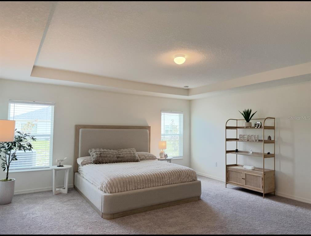 A bedroom features a neutral upholstered bed, two windows, a metal shelving unit, and carpeted flooring — 9033 HOOTON WAY, DAVENPORT, FL