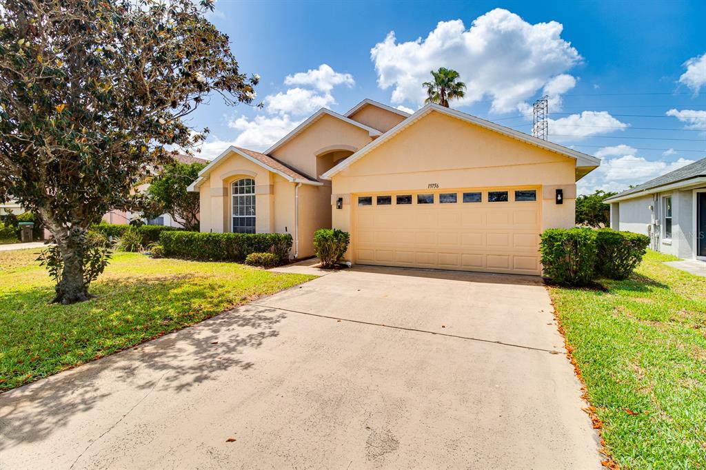 A single-story house with a beige stucco exterior, a two-car garage, and a concrete driveway — 19756 GLEN ELM WAY, ORLANDO, FL
