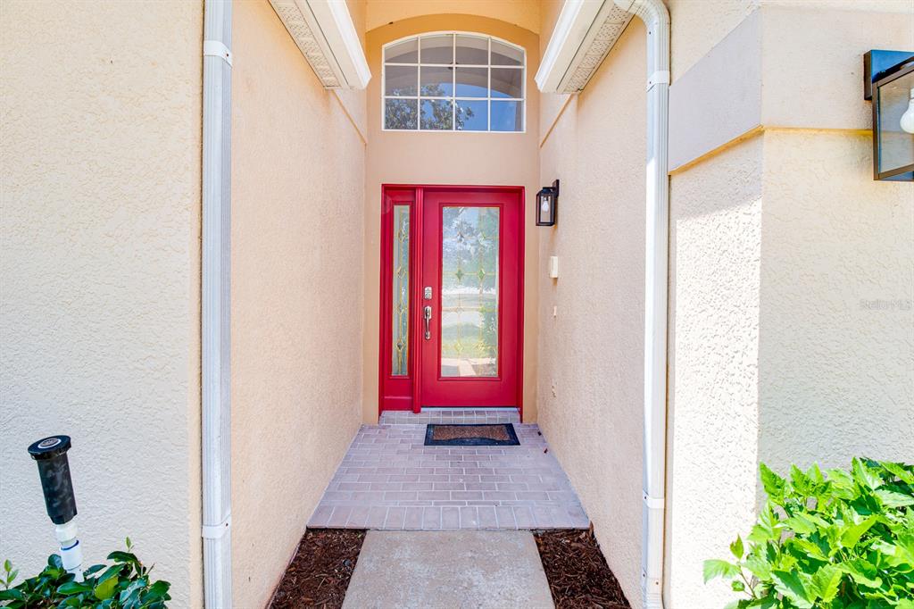 A red front door with a glass panel and sidelight sits under a arched window — 19756 GLEN ELM WAY, ORLANDO, FL