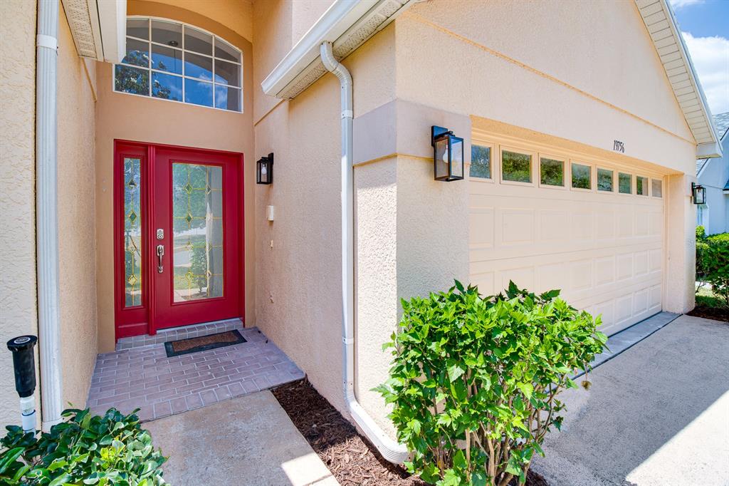 A red front door with a glass insert sits beside a beige garage with windows — 19756 GLEN ELM WAY, ORLANDO, FL