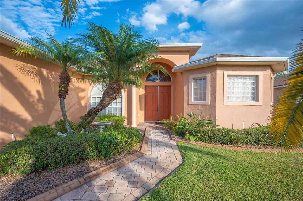 A peach-colored house with a brick walkway, palm trees, and a double front door — 4632 TURNBERRY LANE, LAKE WALES, FL