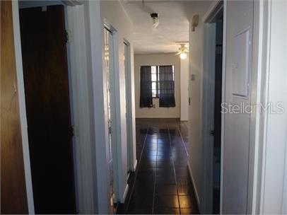 A hallway with dark tile flooring leads toward a room with a window and curtains — 1723 SW 68TH TERRACE, GAINESVILLE, FL